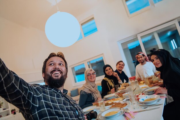 Família muçulmana Eid Mubarak jantando Iftar tirando fotos com smartphone enquanto come comida tradicional durante o mês de festa do Ramadã em casa. A família islâmica Halal comendo e bebendo.