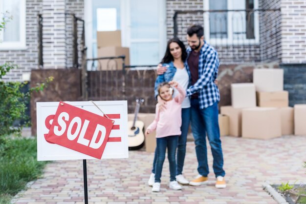 Foto familia mudándose a una casa nueva con letrero vendido en primer plano