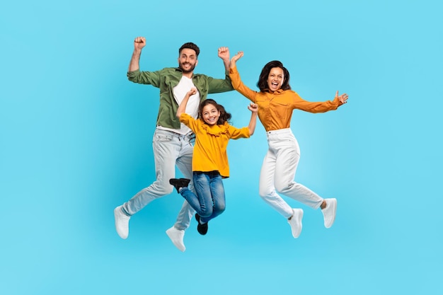 Foto família muito feliz de três pulando gesticulando sim e sorrindo pais e filha posando juntos em