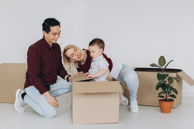 Familia multicultural feliz, padre asiático y madre caucásica con su pequeño hijo desempaquetar cajas en casa nueva. Nuevo edificio residencial casa compra apartamento concepto.