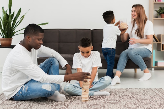 Foto família multicultural jogando um jogo da torre de madeira em casa