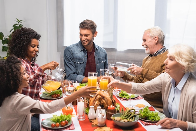 familia multicultural tintineando vasos con bebidas durante la celebración del día de acción de gracias