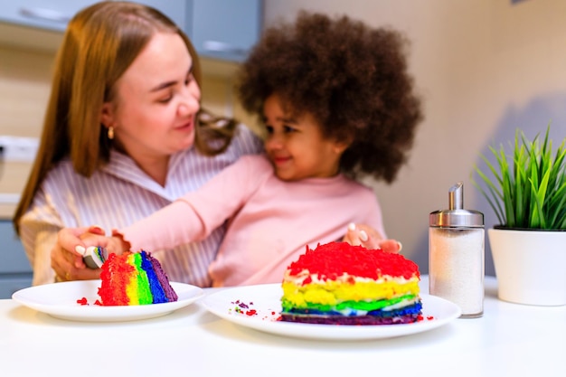 Familia multiétnica feliz comiendo pastel de arco iris en la cocina