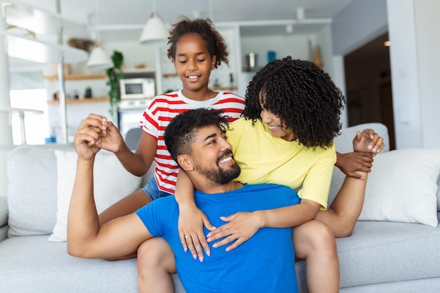 Família multiétnica sentada no sofá na sala de estar em casa aproveita o tempo livre juntos no fim de semana se comunicando uma com a outra Linda filha abraça a mãe se diverte com os pais dentro de casa