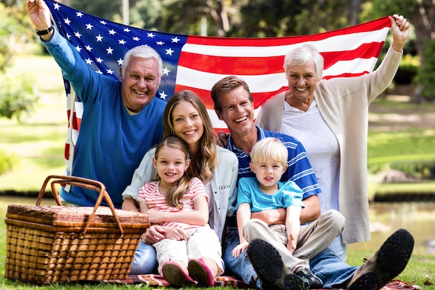 Familia multigeneración que sostiene la bandera americana en el parque