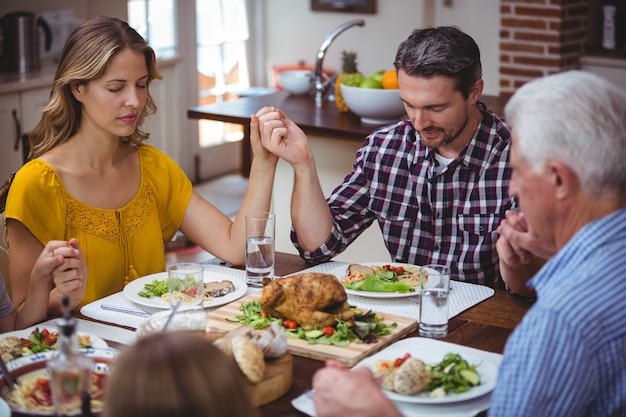 Familia de múltiples generaciones cogidos de la mano mientras reza