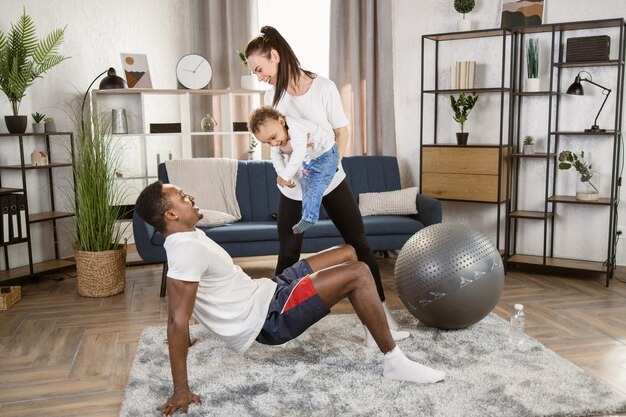 Familia multirracial motivada haciendo ejercicio juntos en casa hombre africano y mujer caucásica con hijo