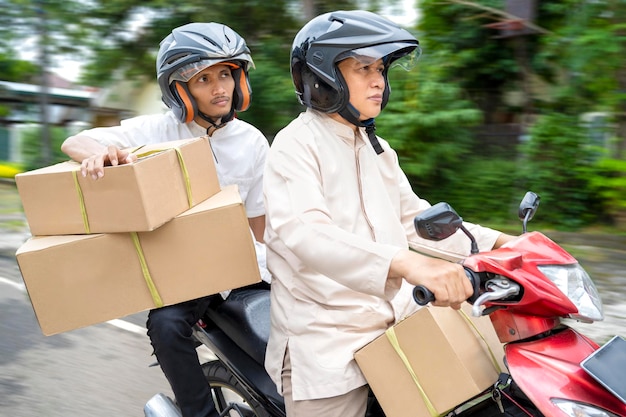 Familia musulmana asiática que lleva una caja en una motocicleta que va mudik