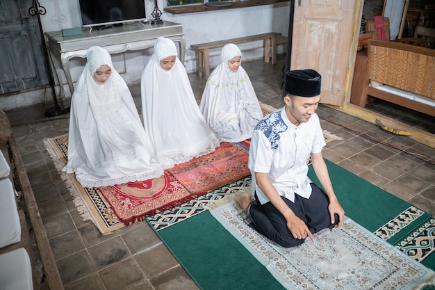 Familia musulmana asiática rezando jamaah juntos en casa. sholat o salah vestidos de blanco y hijab