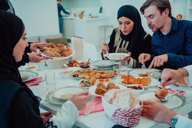 Familia musulmana cenando Iftar bebiendo agua para romper la fiesta. Comer comida tradicional durante el mes de fiesta del Ramadán en casa. La comida y bebida halal islámica en el hogar moderno.