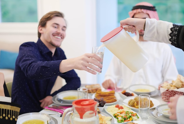 Familia musulmana de Eid Mubarak cenando Iftar bebiendo agua para romper la fiesta. Comer comida tradicional durante el mes de fiesta del Ramadán en casa. La comida y bebida halal islámica en la isla occidental moderna