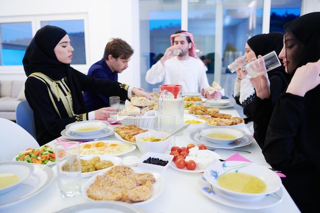 Familia musulmana de Eid Mubarak cenando Iftar bebiendo agua para romper la fiesta. Comer comida tradicional durante el mes de fiesta del Ramadán en casa. La comida y bebida halal islámica en la isla occidental moderna