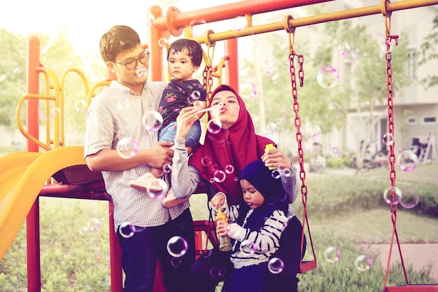 Familia musulmana jugando jabón de burbujas en el patio de recreo