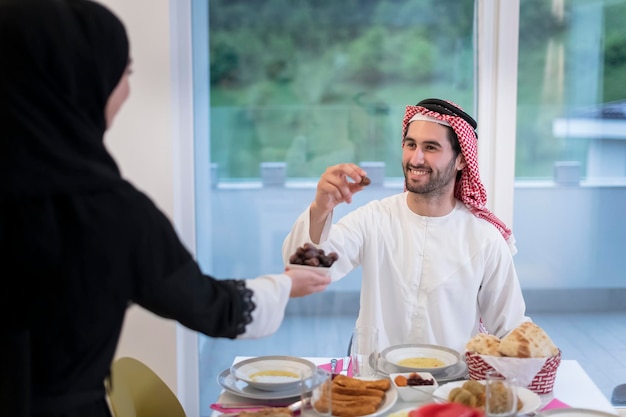 familia musulmana multiétnica moderna que comparte un tazón de dátiles mientras disfruta de una cena iftar juntos durante una fiesta de Ramadán en casa.