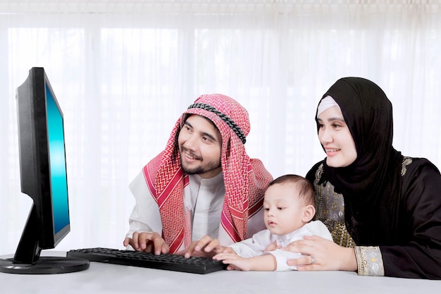 Familia musulmana de padre, madre e hijo usando una computadora en línea en casa