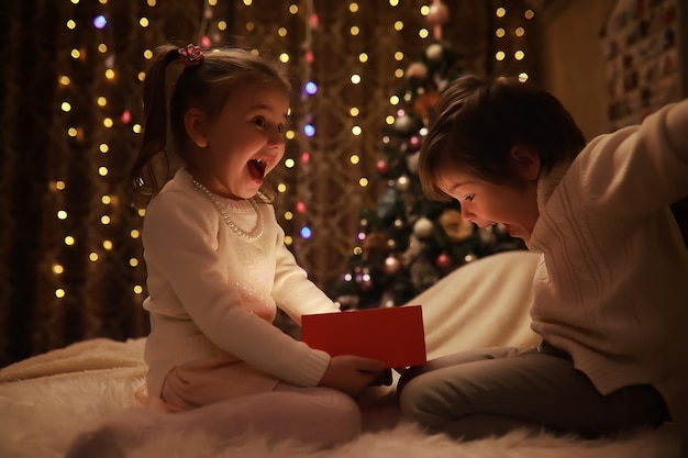 Família na véspera de natal na lareira. crianças abrindo presentes de natal. crianças debaixo da árvore de natal com caixas de presente. sala decorada com lareira tradicional. aconchegante noite de inverno quente em casa.