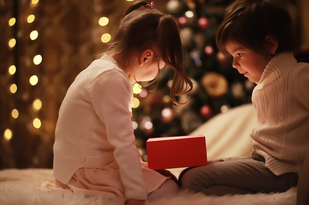 Família na véspera de Natal na lareira. Crianças abrindo presentes de Natal. Crianças debaixo da árvore de Natal com caixas de presente. Sala decorada com lareira tradicional. Aconchegante noite quente de inverno em casa.