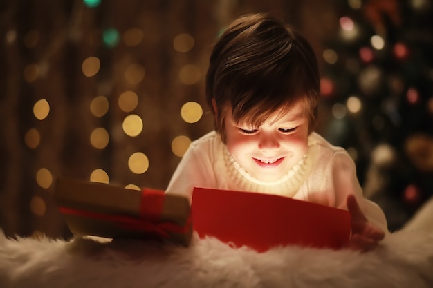 Família na véspera de Natal na lareira. Crianças abrindo presentes de Natal. Crianças debaixo da árvore de Natal com caixas de presente. Sala decorada com lareira tradicional. Aconchegante noite quente de inverno em casa.