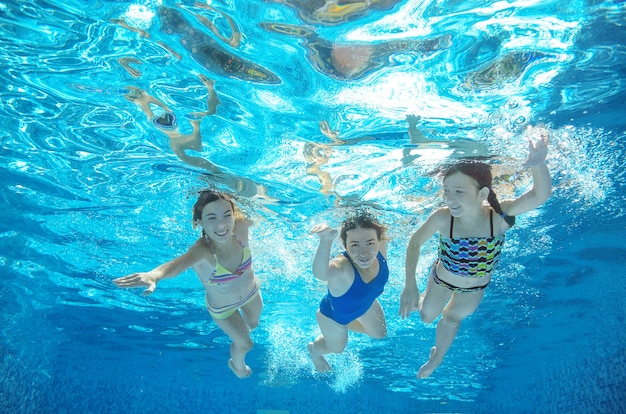 La familia nada en la piscina bajo el agua, la feliz madre activa y los niños se divierten bajo el agua, hacen ejercicio y hacen deporte con los niños en las vacaciones de verano en el resort