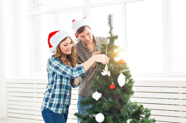 Família, Natal, férias de inverno e conceito de pessoas - jovem casal feliz decorando a árvore de Natal em casa.