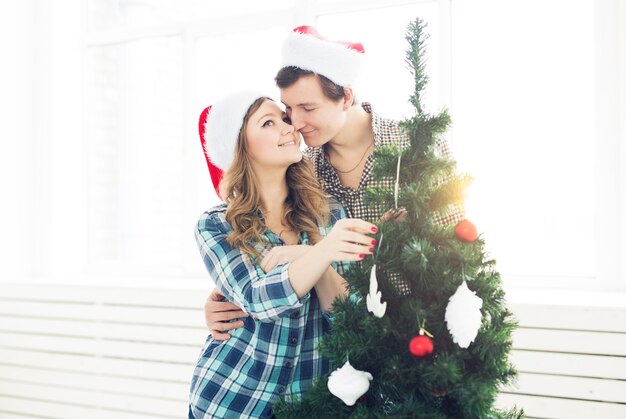 Família, Natal, férias de inverno e conceito de pessoas - jovem casal feliz decorando a árvore de Natal em casa.