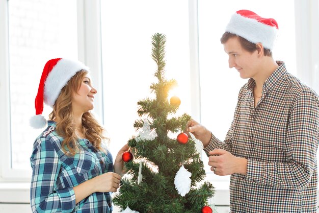 Família, Natal, férias de inverno e conceito de pessoas - jovem casal feliz decorando a árvore de Natal em casa.