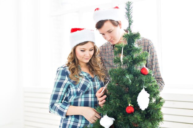 família, natal, férias de inverno e conceito de pessoas - jovem casal feliz decorando a árvore de natal em