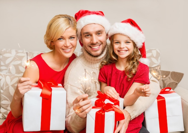 família, natal, natal, inverno, felicidade e conceito de pessoas - família sorridente com chapéus de ajudante de Papai Noel com muitas caixas de presente e luzes de bengala