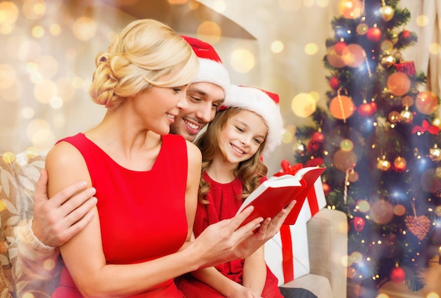 família, natal, natal, inverno, felicidade e conceito de pessoas - família sorridente com chapéus de ajudante de Papai Noel com muitas caixas de presente lendo livro