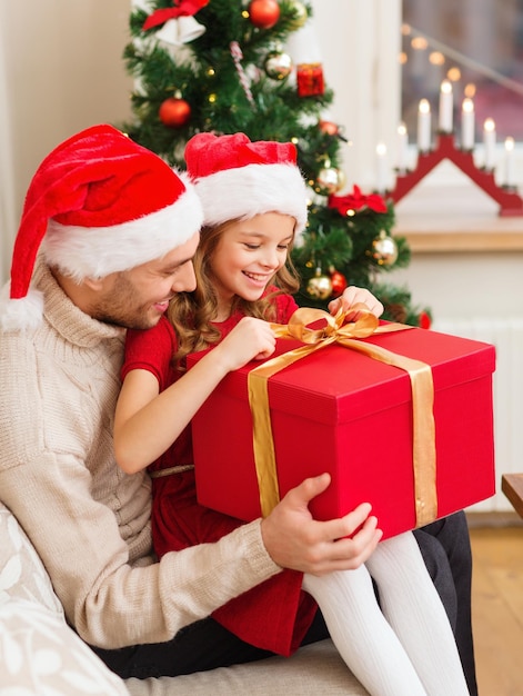 família, natal, natal, inverno, felicidade e conceito de pessoas - sorrindo pai e filha em chapéus de ajudante de Papai Noel abrindo a caixa de presente