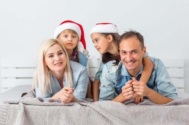 Familia de Navidad acostado en la cama blanca con sombreros rojos. Niños y padres felices