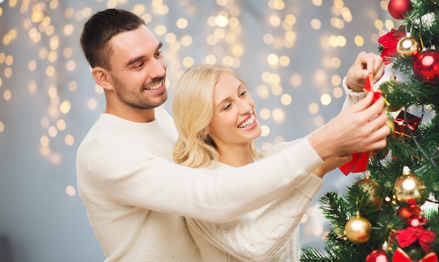 familia, navidad, vacaciones de invierno y concepto de la gente - pareja feliz decorando el árbol de navidad sobre fondo de luces