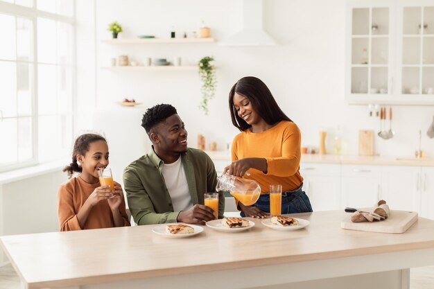 Familia negra almorzando bebiendo jugo de naranja fresco en la cocina