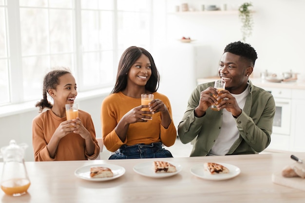 Familia negra bebiendo jugo de naranja disfrutando del desayuno sentado en la cocina