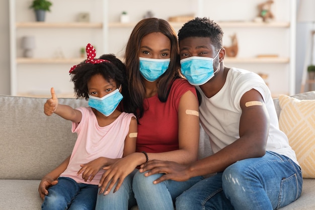 Família negra de três usando máscaras médicas posando em casa após a vacinação