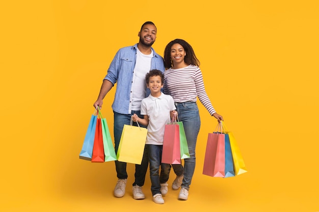 Una familia negra encantada disfrutando haciendo compras juntos sosteniendo coloridas bolsas de papel