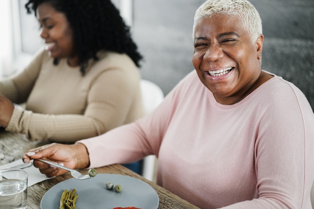 Foto família negra feliz almoçando em casa. mãe e filha se divertindo sentadas à mesa de jantar