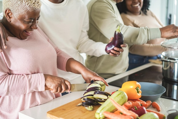 Família negra feliz cozinhando dentro da cozinha em casa concentre-se na mão esquerda segurando a faca