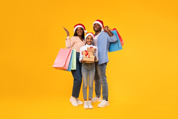 Familia negra feliz sosteniendo bolsas de compras y cajas de regalo de Navidad
