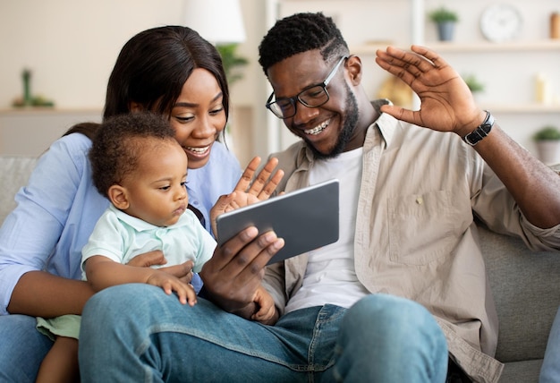 Família negra feliz tendo videochamada usando tablet acenando com as mãos