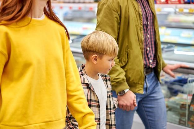 Familia con niño niño comprando juntos en la tienda de comestibles, hombre mujer y niño disfrutan caminando en el supermercado, comprando productos, se dan la mano juntos
