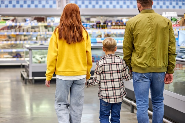 Familia con niño niño comprando juntos en la tienda de comestibles, hombre mujer y niño disfrutan caminando en el supermercado, comprando productos. vista trasera