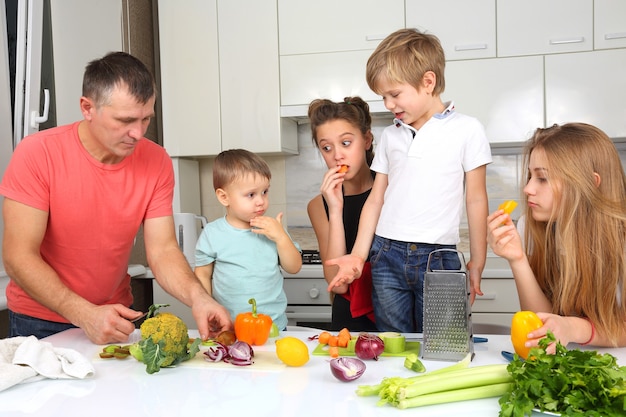 Familia con niños cortar verduras para cocinar