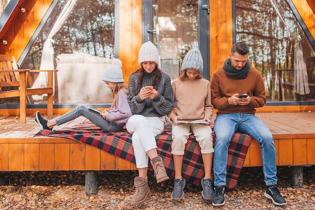 Familia con niños en el día de otoño, cada uno con su propio dispositivo al aire libre