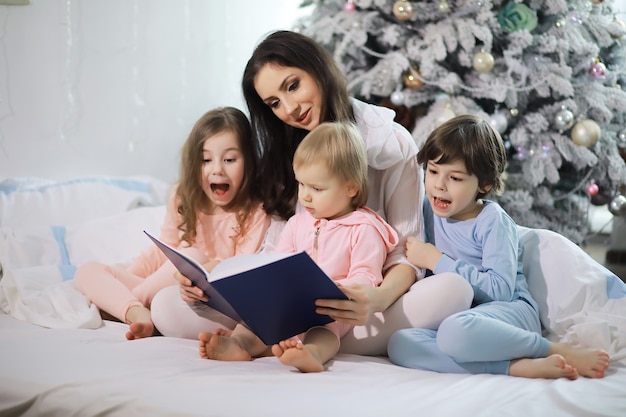 Una familia con niños divirtiéndose en la cama bajo las mantas durante las vacaciones de Navidad.