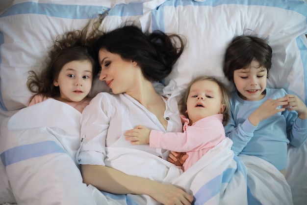 Una familia con niños divirtiéndose en la cama bajo las mantas durante las vacaciones de Navidad.