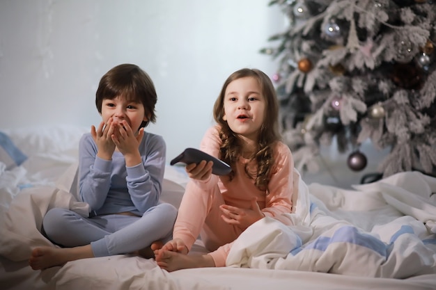 Una familia con niños divirtiéndose en la cama bajo las mantas durante las vacaciones de Navidad.