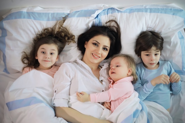 Una familia con niños divirtiéndose en la cama bajo las mantas durante las vacaciones de Navidad.