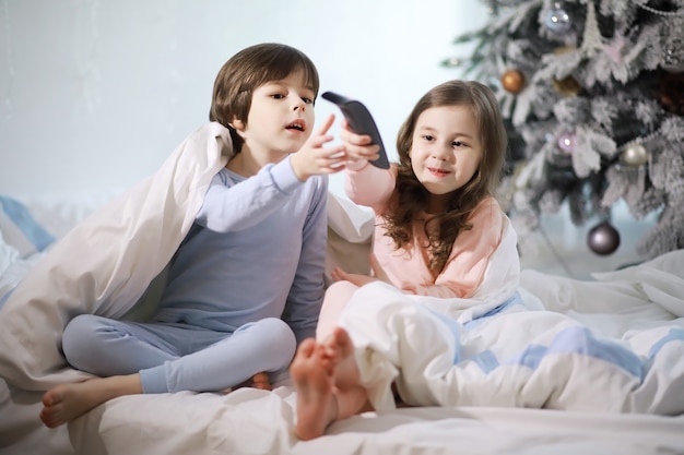 Una familia con niños divirtiéndose en la cama bajo las mantas durante las vacaciones de Navidad.