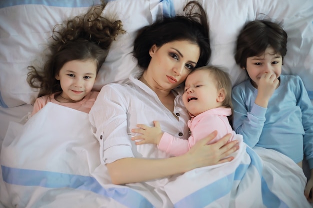 Una familia con niños divirtiéndose en la cama bajo las mantas durante las vacaciones de Navidad.